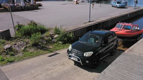 Vista-Aérea-Alrededor-Del-Automóvil-Y-El-Remolque,-Levantando-Un-Bote-En-Un-Muelle,-Día-De-Verano,-En-Finlandia---Dando-Vueltas,-Disparo-Con-Drones