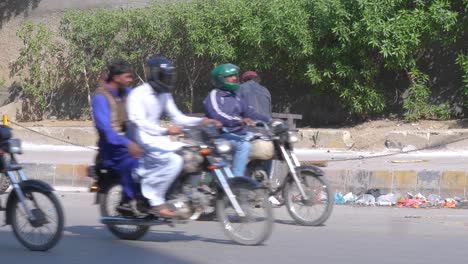 Toma-Trasera-De-Un-Basurero-Recogiendo-Basura-Del-Cubo-De-Basura-Que-Se-Encuentra-Al-Lado-De-Una-Calle-Muy-Transitada-En-La-Calle-Saddar-Bazar-De-Karachi,-Pakistán,-Durante-La-Tarde.