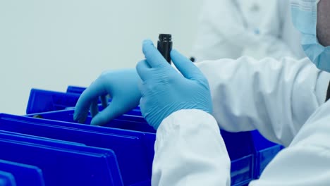 Lab-technician-in-lab-jacket-and-blue-medical-gloves-packs-cannabis-pre-rolls-into-a-tube-that-will-be-sold-in-dispensaries