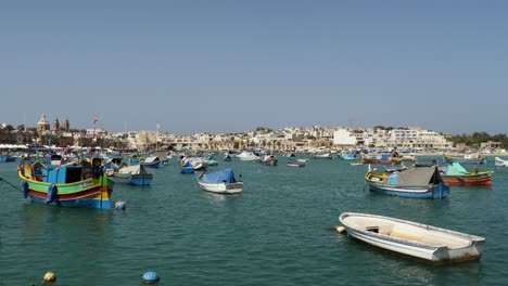 Bunte-Boote-Schwimmen-Im-Hafen-Von-Marsaxlokk-Mit-Gebäuden-Im-Hintergrund