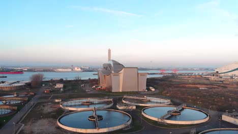 Aerial-of-Crossness-Sewage-Treatment-Works,-with-the-Thames-River-and-Boats-in-the-background