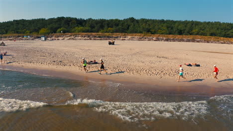 Drohne-Fliegt-über-Läufern,-Die-An-Sonnigen-Sommertagen-Am-Strand-Laufen