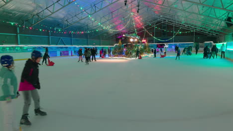 Niños-Patinando-En-Una-Pista-De-Hielo-Cubierta-Alrededor-De-Una-Escena-Festiva