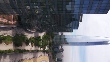 Vista-Aérea-Del-Rascacielos-De-Oficinas-Reflectante-Con-Plataforma-Rodante-A-La-Derecha-Para-Revelar-La-Gran-Torre-Santiago-En-El-Fondo