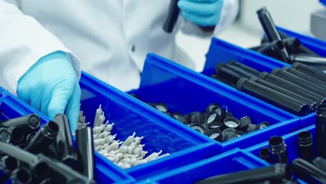 Lab-technician-in-lab-jacket-and-blue-medical-gloves-on-the-assembly-line-packs-cannabis-pre-rolls-into-a-tube-that-will-be-sold-in-dispensaries