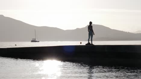 Silhouetted-figure-of-a-woman-welcomes-sunrise-on-a-pier,-embracing-sun's-warmth-in-meditation