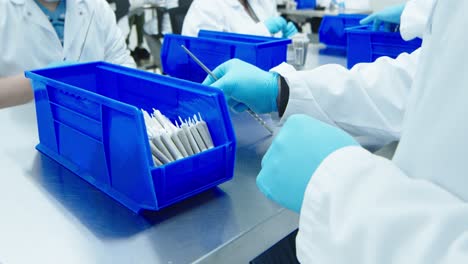 Over-the-should-shot-of-lab-technician-in-lab-jacket-and-blue-medical-gloves-tamps-and-twists-cannabis-pre-rolls-and-places-them-into-full-bin