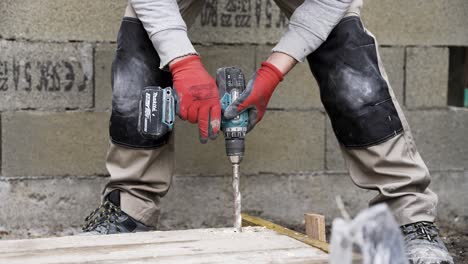 Bauarbeiter-Bohrt-Mit-Einer-Bohrmaschine-Ein-Großes-Loch-In-Die-Ecke-Eines-Holzbretts-Und-Trägt-Handschuhe,-Mittlere-Aufnahme