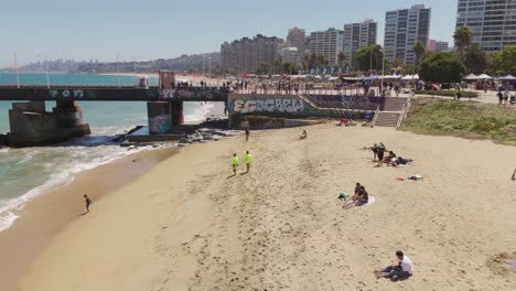 Aerial-Flying-Low-Over-Acapulco-Beach-Towards-Vergara-Pier-In-Vina-Del-Mar-On-Sunny-Day-With-Beachgoers-Below