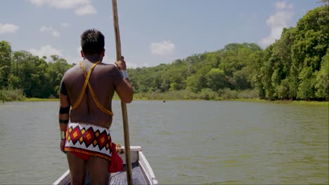 Hombre-Tribal-Parado-En-Un-Bote-En-Un-Río-Con-Traje-Trible-Y-Un-Palo-En-La-Mano-Panamá,-Río-Chagres,-Hombre-Indio-Embera-Parado-Frente-A-Una-Canoa