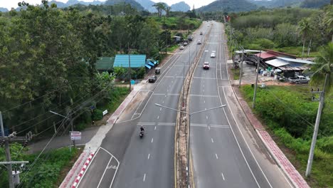 Toma-Aérea-De-Una-Niña-Montando-Una-Scooter-En-Una-Carretera-Rodeada-De-Vegetación-En-Tailandia