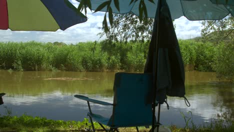 Ein-Stuhl-Und-Ein-Sonnenschirm-Am-Fluss-Beim-Angeln-An-Einem-Sonnigen-Tag