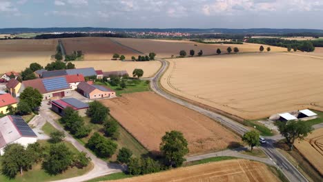 Toma-Aérea-De-Seguimiento-De-Un-Automóvil-Conduciendo-Por-Campos-Y-Edificios-Agrícolas.