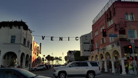 Toma-Panorámica-Del-Cartel-De-Venecia-En-La-Esquina-De-Pacific-Ave---Windward-Ave-Con-Tráfico,-Durante-La-Puesta-De-Sol,-En-Los-Ángeles,-California,-EE.UU.