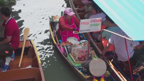 Plano-Medio,-Mujeres-Con-Delantal-Rosa-Vendiendo-Pollo-Frito-Y-Camarones-A-Turistas-En-El-Mercado-Flotante-De-Tailandia.