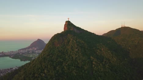 Drone-Vuela-Hacia-Cristo-Redentor-Durante-La-Hora-Dorada-Con-La-Ciudad-De-Río-En-La-Distancia