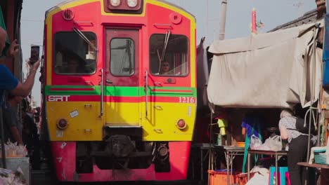 Establishing-shot,-Elderly-women-tourist-takes-photo-of-the-approaching-train-in-Maeklong-Samut-Rail-Road-Market-Thailand