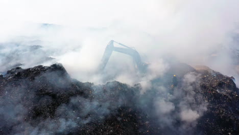 Aerial-view-of-a-excavator-clearing-a-area-on-fire,-caused-by-a-bomb,-dark-smoke-rising,-war-and-terror-in-Middle-east,-Asia---Still,-drone-shot