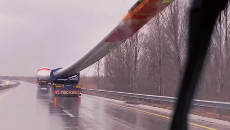 POV-De-Un-Automóvil-Conduciendo-Por-La-Autopista-En-Un-Día-Lluvioso-Con-Un-Enorme-Ventilador-De-Molino-Pasando-Sobre-El-Camión