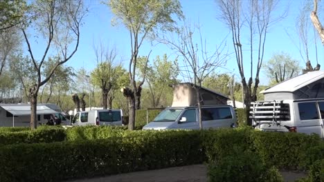 Camping-Parkplace-with-some-campers-and-bus-parked-within-trees-and-bushes-in-the-middle-of-nature