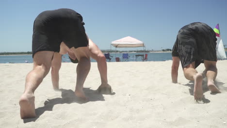 Atletas-Masculinos-Haciendo-Ejercicio-De-Rastreo-De-Osos-En-La-Playa-Con-El-Océano-Pacífico-En-Segundo-Plano.