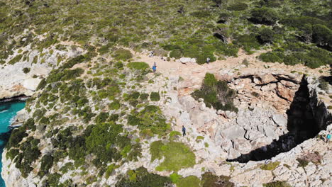 Backward-flying-drone-shot-over-a-sea-arch-with-a-few-tourists-walking-around-near-Cala-Varques-beach-in-Majorca