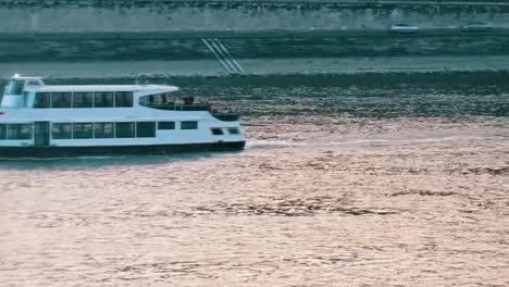 Passenger-Boats-Going-By-On-River-With-Traffic-On-Roads-In-The-Background