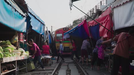 Kamerafahrt:-Verkäufer-Bauen-Ihr-Geschäft-Auf-Dem-Maeklong-Samut-Rail-Road-Markt-In-Thailand-Auf,-Im-Hintergrund-Fährt-Ein-Zug-An-Der-Eisenbahnstrecke-Vorbei