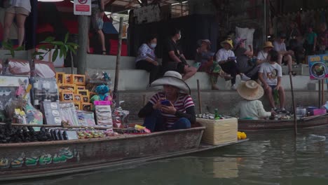 Toma-De-Vista-Lateral-Avanzando,-Vista-Panorámica-Del-Mercado-Flotante-En-Tailandia,-Gente-Sentada-En-Los-Escalones-Del-Fondo