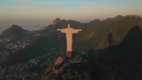 Drone-Vuela-Hacia-Atrás-Desde-Cristo-Redentor-Durante-La-Hora-Dorada-Con-La-Ciudad-De-Río-En-La-Distancia