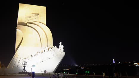 Padrão-Dos-Descobrimentos-Monumento-Marítimo-Con-El-Puente-25-De-Abril-Y-El-Santuario-Iluminado-De-Cristo-Rey-Al-Fondo,-Lisboa,-Portugal