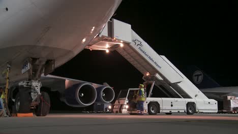 Nächtliche-Flughafenszene-Mit-Frachtverladung-In-Ein-Flugzeug-über-Eine-Beleuchtete-Flugtreppe