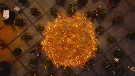 Árbol-De-Navidad-En-La-Plaza-Con-Gente-Y-Otros-árboles-Pequeños-Por-La-Noche---Vista-De-Arriba-Hacia-Abajo