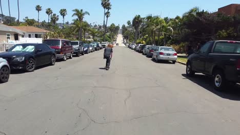 Stylish-young-male-with-long-hair-skating-down-the-street-in-Southern-California-beach-town