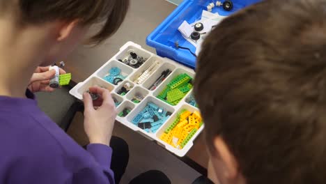 A-pair-of-boys-working-together-to-assemble-pieces-of-a-robotic-car-next-to-a-laptop-in-a-technology-class