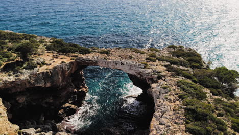 Upward-flying-drone-shot-of-a-sea-arch-with-tourists-walking