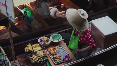 Down-to-zoom-out-shot,-Fried-Shrimp-and-Chicken-bbq-vendor-in-Thailand-floating-market,-cold-beverages-at-the-rear-of-the-boat