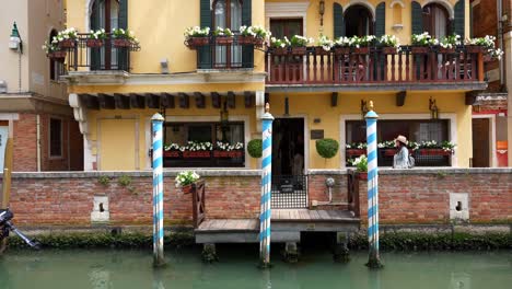 Female-tourist-walks-between-docking-pier-and-yellow-building-in-Venice