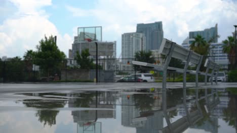 Empty-wet-playground-basketball-court-in-distance-under-urban-skyscraper-business-district-cityscape