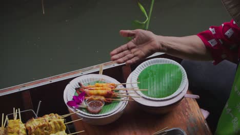 Disparo-De-Alejamiento-Hacia-Abajo,-Camarones-En-Un-Palo-Servidos-Sobre-Hojas-De-Bambú-Preparados-Por-Un-Vendedor-De-Barcos-En-El-Mercado-Flotante-De-Tailandia