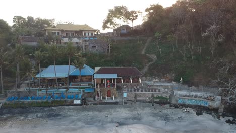 Aerial-shot-of-the-tropical-bay-with-sandy-beach,-tourist-jogging-and-buildings-resort