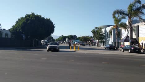 Obdachloser-Bettelt-Auf-Den-Straßen-Von-Venice-Beach,-Während-Ein-Auto-Vorbeifährt,-Sonniger-Tag,-In-Los-Angeles,-Kalifornien,-USA-–-Handaufnahme