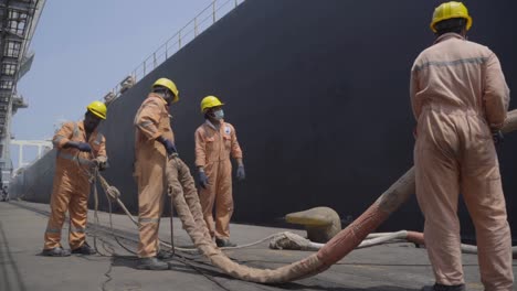 Trabajadores-Portuarios-Sosteniendo-Y-Desenredando-La-Cuerda-De-Amarre-De-Un-Enorme-Buque-En-El-Puerto