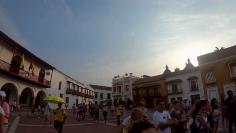 A-tour-guide-with-a-yellow-umbrella-is-walking-near-a-group-of-tourists-that-are-standing-in-the-middle-of-a-plaza-of-the-old-town-of-Cartagena-de-Indias,-Colombia