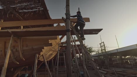 Worker-Climbing-Ladder-At-Dhow-Ship-Building-Yard-In-Sur,-Oman