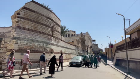 People-walk-in-front-of-Remains-Of-Roman-Tower-By-The-Coptic-Museum,-at-Cairo,-Egypt