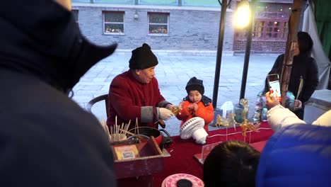 Gubei-Water-Town,-Beijing,-China,-fair-attraction,-a-man-shows-a-kid-the-candy-animal-he-made-by-candy-blowing-technique-in-a-Chinese-New-Year-fair