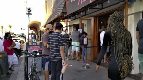 Masked-people-waiting-in-line-for-food,-at-a-restaurant,-sunny-day,-in-Los-Angeles,-California,-USA---Static-shot