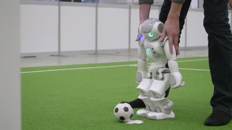 Ingeniero-Sosteniendo-Los-Hombros-Del-Robot-Nao-Mientras-Camina-Para-Patear-La-Pelota