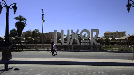 Turistas-Caminando-Frente-Al-Cartel-De-La-Ciudad-De-Luxor-En-Egipto